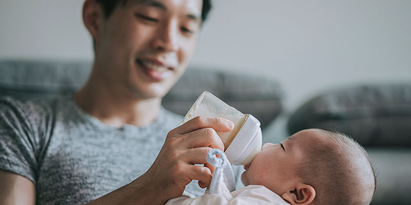 A young Asian man bottle feeding a baby.