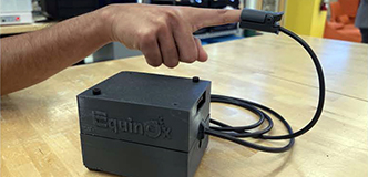 The EquinOx device is attached to a pulse oximeter, which is attached to someone’s finger. 