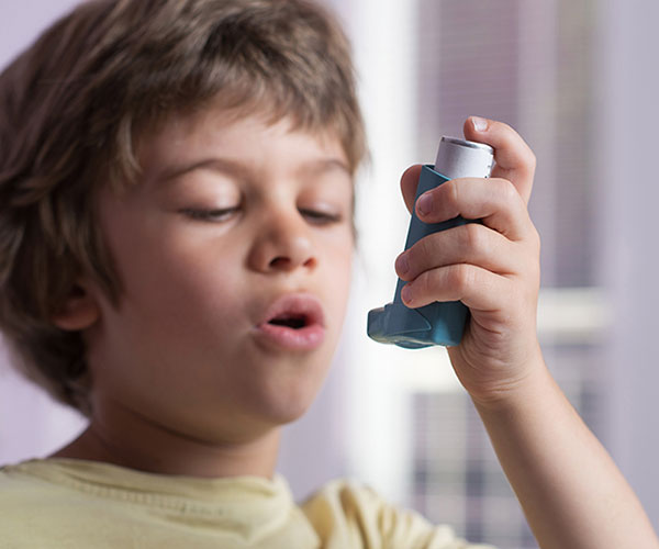 A young boy holds an asthma inhaler in his hand.