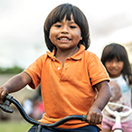 A boy and girl are riding bicycles. The scenery is blurred but appears rural.