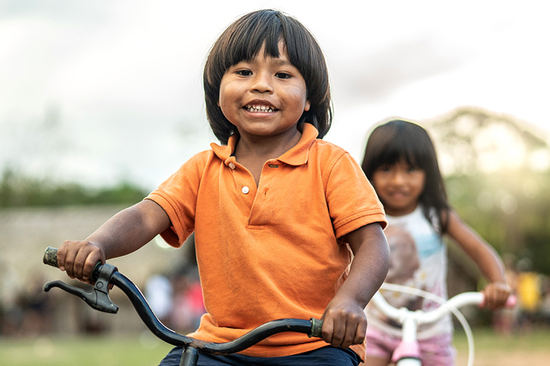 A boy and girl are riding bicycles. The scenery is blurred but appears rural.