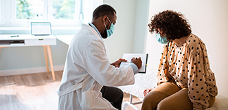 Patient seated on examination table facing medical professional holding a clipboard.