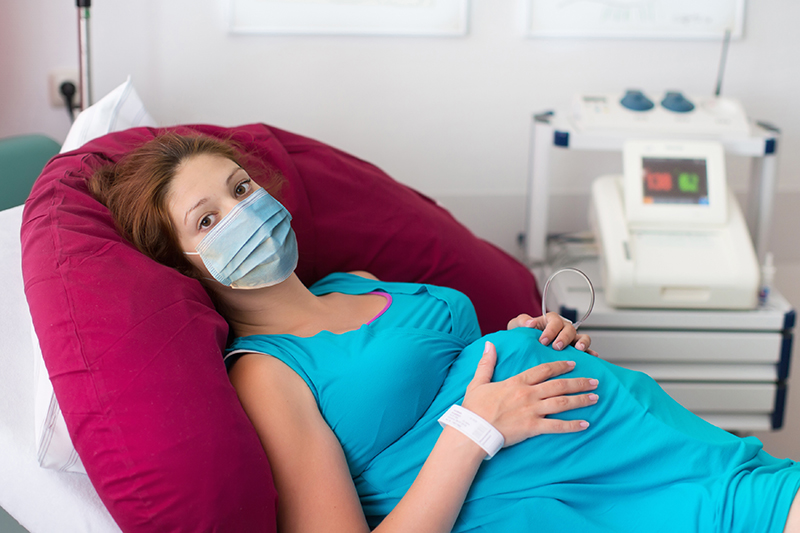 Pregnant person, masked, on their back in a hospital setting.