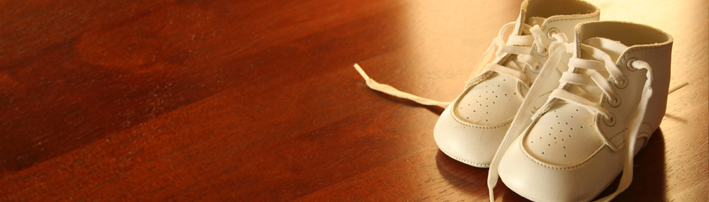 A pair of white baby shoes setting on a hardwood floor.