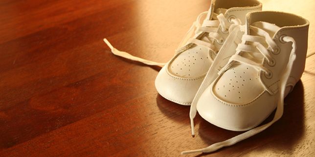 A pair of white baby shoes setting on a hardwood floor. 
