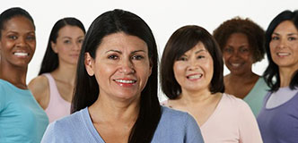 Group of women of different ethnicities and sizes standing together and smiling at the camera.