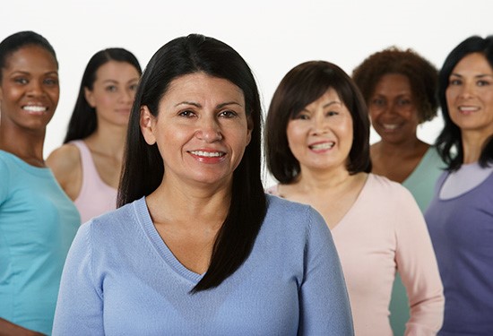 Group of women of different ethnicities and sizes standing together and smiling at the camera.