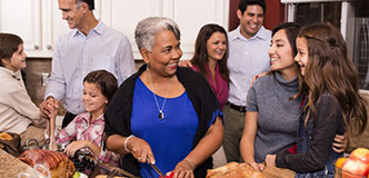 Multi-ethnic, multi-generational family members prepare a holiday dinner together in their home kitchen.