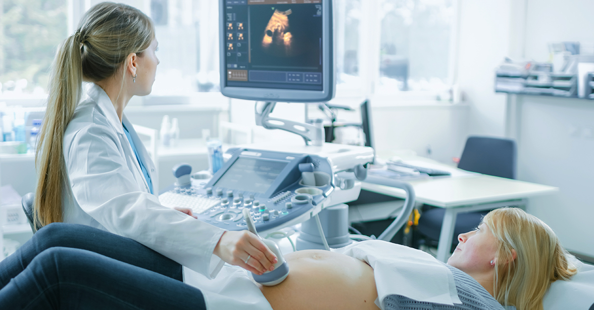 A healthcare provider uses an ultrasound machine on a pregnant parent’s belly as they both watch the screen in the hospital room.