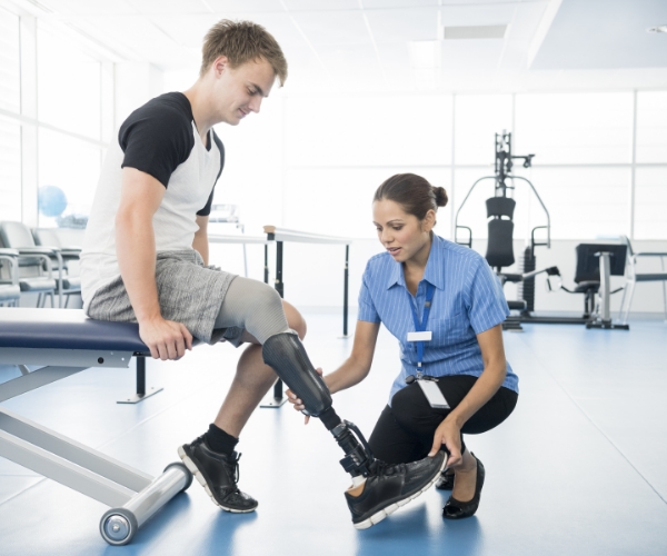 A healthcare provider, who is crouched on the ground, adjusts a man’s prosthetic leg. 