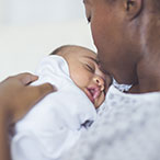 A Black woman wearing a hospital gown kisses the forehead of her newborn baby.