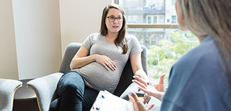 Pregnant person talking to medical professional holding a notebook.