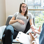 Pregnant person talking to medical professional holding a notebook.