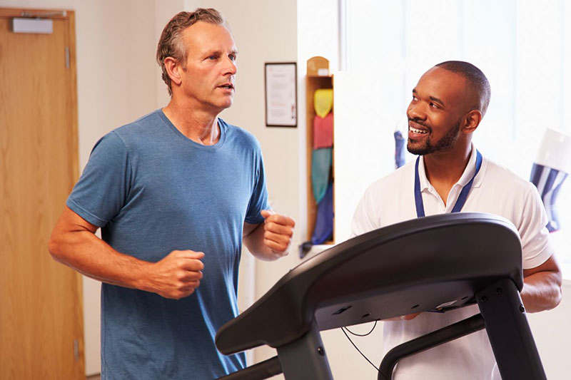 Patient on treadmill while medical professional looks on.