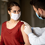 Health care worker swabbing a woman's arm. Both are wearing masks. 