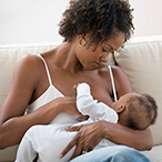 Mother sitting on a couch breast feeding a baby she holds in her lap.