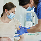Pregnant woman receiving an injection in the arm from a health care provider. Both are masked.