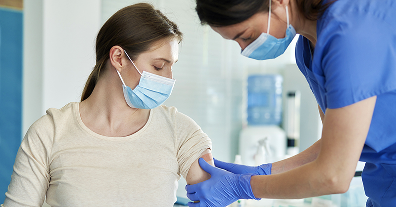 Pregnant woman receiving an injection in the arm from a health care provider. Both are masked.