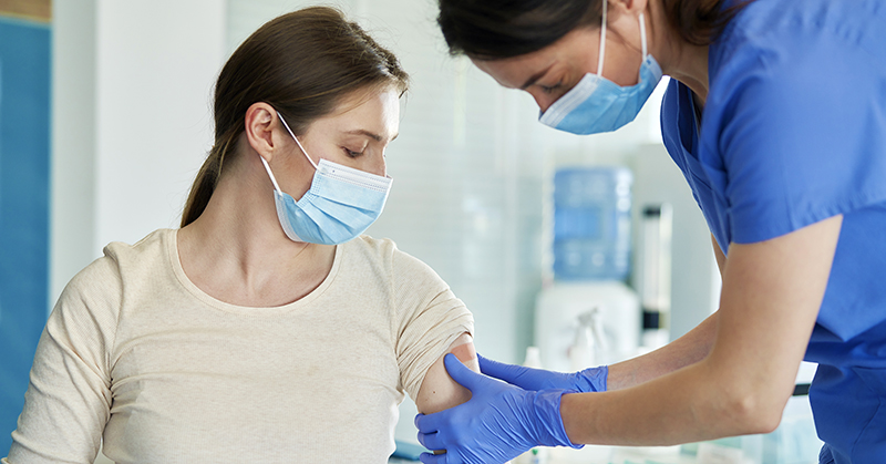 Pregnant person receiving an injection in the arm from a health care provider. Both are masked.