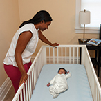 Parent leaning over crib containing infant asleep on their back.