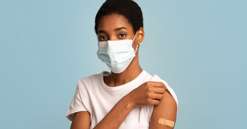 Woman pulling up sleeve to show band aid on shoulder.