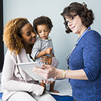 A health care provider shows a digital tablet to a mother holding a child.