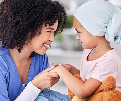 A health care provider smiles at a young patient while holding her hands. The girl is wearing a headscarf.