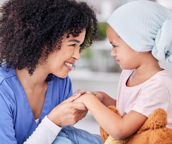 A health care provider smiles at a young patient while holding her hands. The girl is wearing a headscarf.