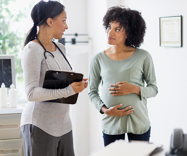 A pregnant person speaking to a health care provider in a medical office.