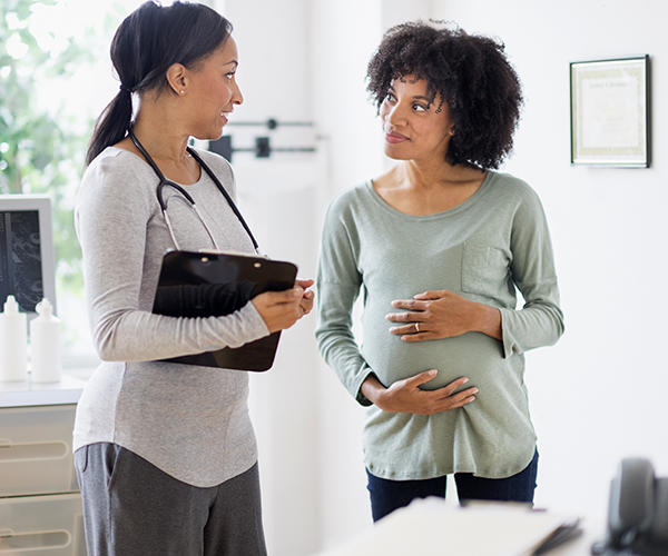 A pregnant woman speaking to a health care provider in a medical office.