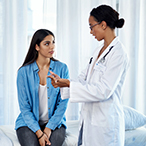 Patient, sitting on examination table, listening, while health care provider talks.