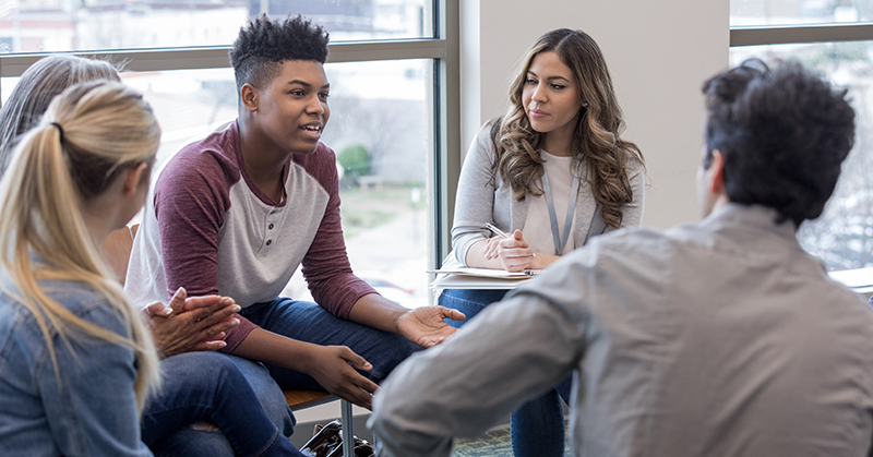 A diverse group of young adults sitting in a circle talking.