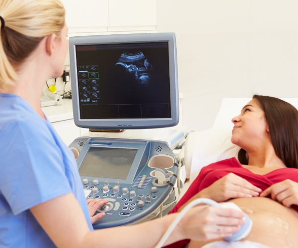 A health care provider giving a pregnant person an ultrasound in a medical office.
