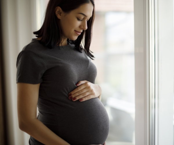 A pregnant person looking at their belly in front of a window.