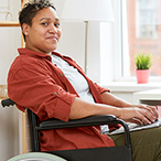 A woman smiles while seated in a wheelchair with a laptop.