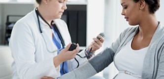 Health care provider taking blood pressure reading of pregnant person.