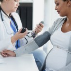 Health care provider taking blood pressure reading of pregnant woman.