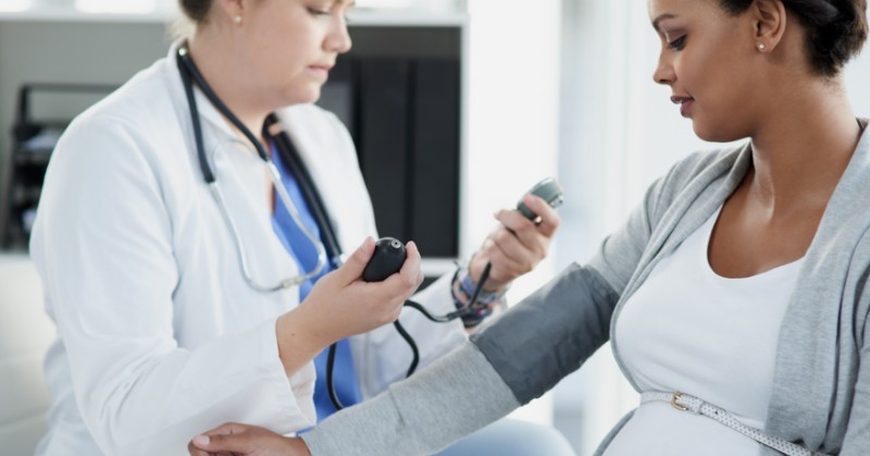 Health care provider taking blood pressure reading of pregnant person.