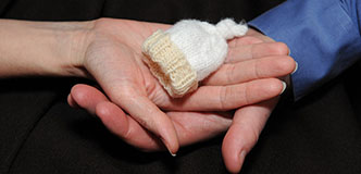 Hands of a couple holding a hat sized for a premature newborn.