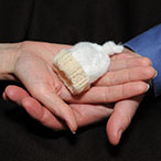 Hands of a couple holding a hat sized for a premature newborn.