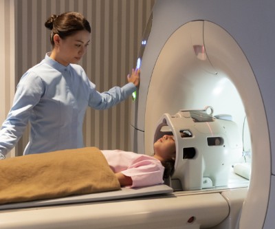 An MRI technician looks over a young girl who is laying down on an MRI scanner. 