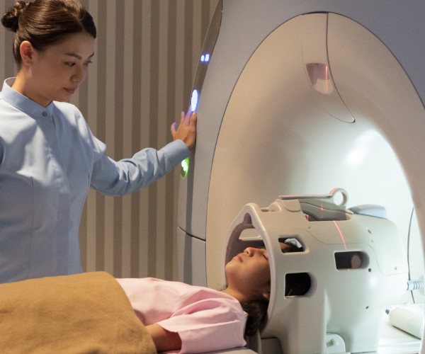 An MRI technician looks over a young girl who is laying down on an MRI scanner. 