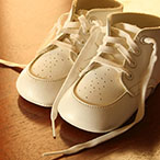 A pair of white baby shoes setting on a hardwood floor.