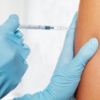 Gloved hands giving an injection in an upper arm.