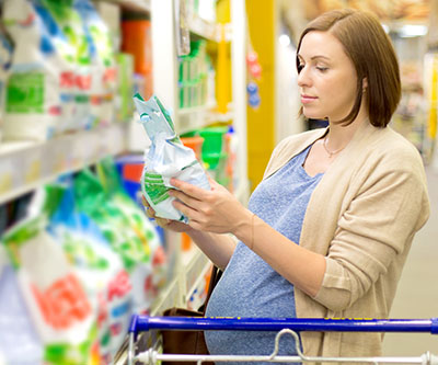 A pregnant woman stands in the aisle of a store examining a package of detergent. 
