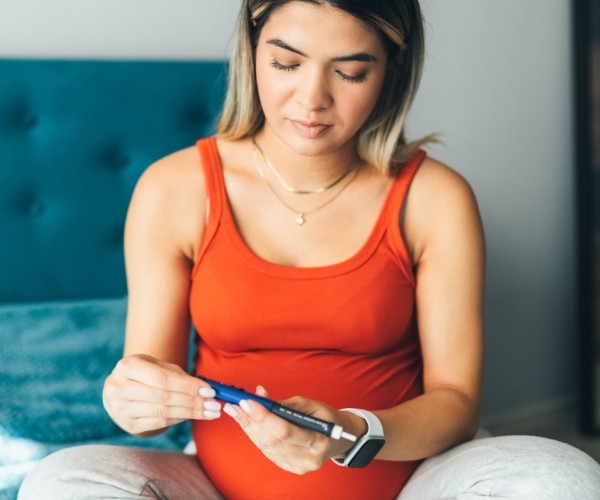 A pregnant woman sits on a bed and prepares insulin dosage on insulin pen.