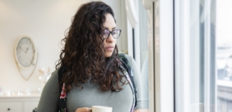 Pregnant person holding a cup, looking out a window.