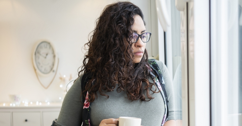 Pregnant woman holding a cup, looking out a window.