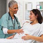 A pregnant woman sits up on a hospital bed and is speaking with a health care provider. 