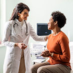 A woman in a doctor’s office is sitting down while speaking to a health care provider.